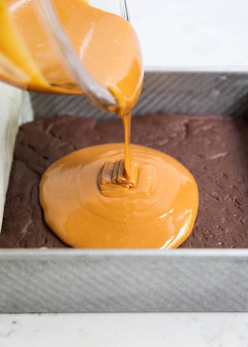 pouring caramel over fudge in pan 