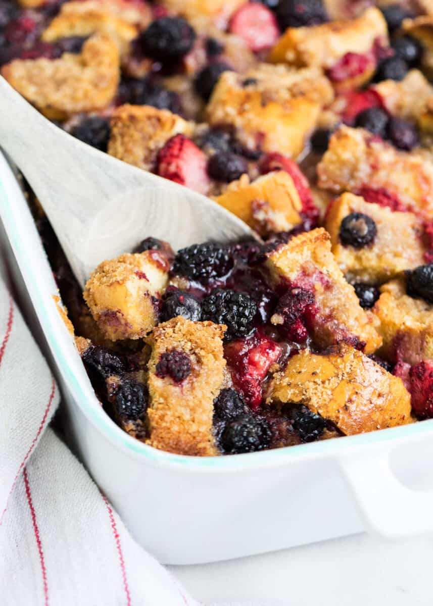 scooping out berry overnight french toast with a wooden spoon 