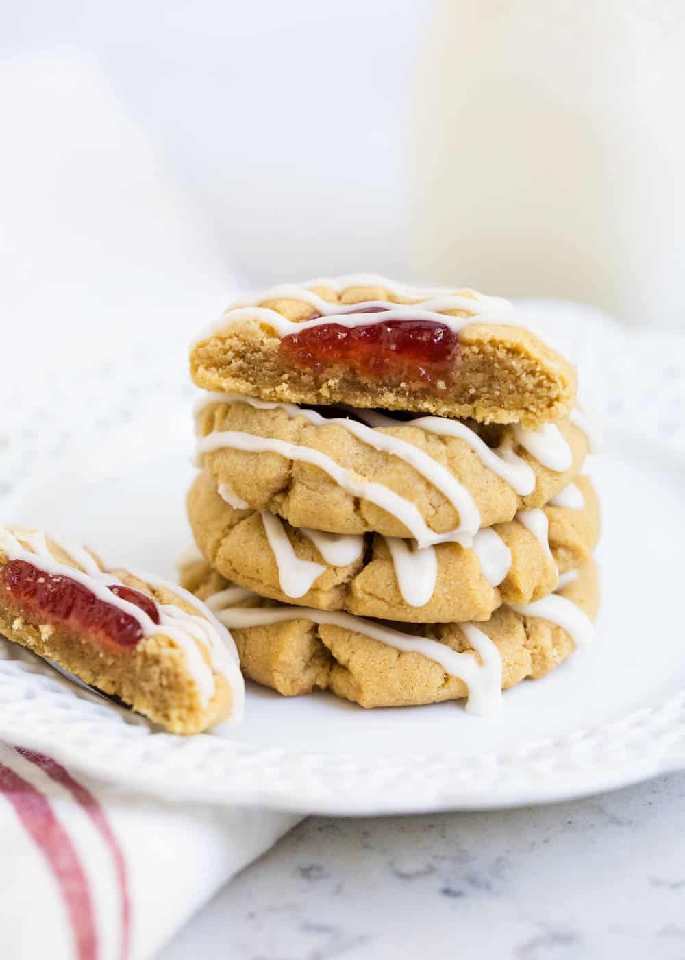 Stacked peanut butter and jelly cookies on white plate.