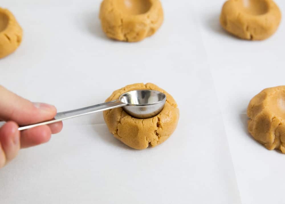 Making a thumbprint in a peanut butter cookie with a teaspoon.