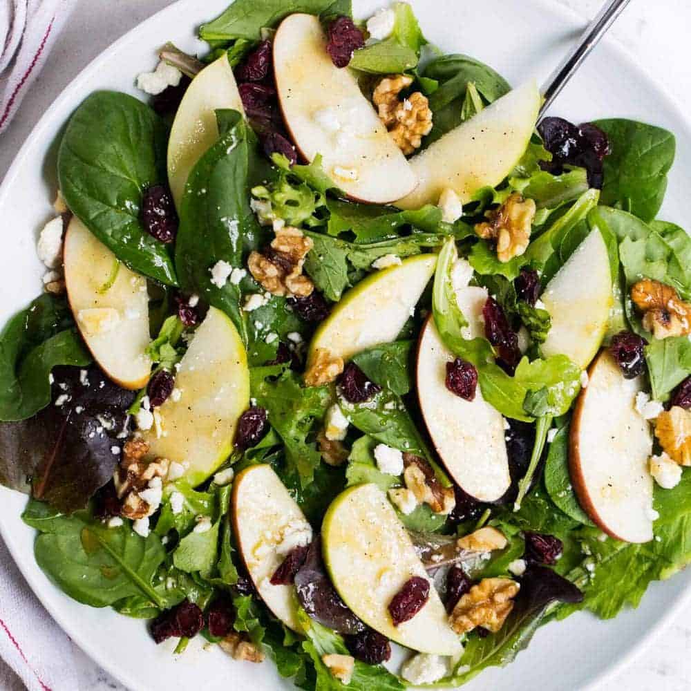 Apple cranberry spinach salad filled with greens, crisp apples, dried cranberries, walnuts, feta cheese and a delicious honey dijon dressing. An easy salad recipe that's full of flavor! Spinach salad on a white plate.