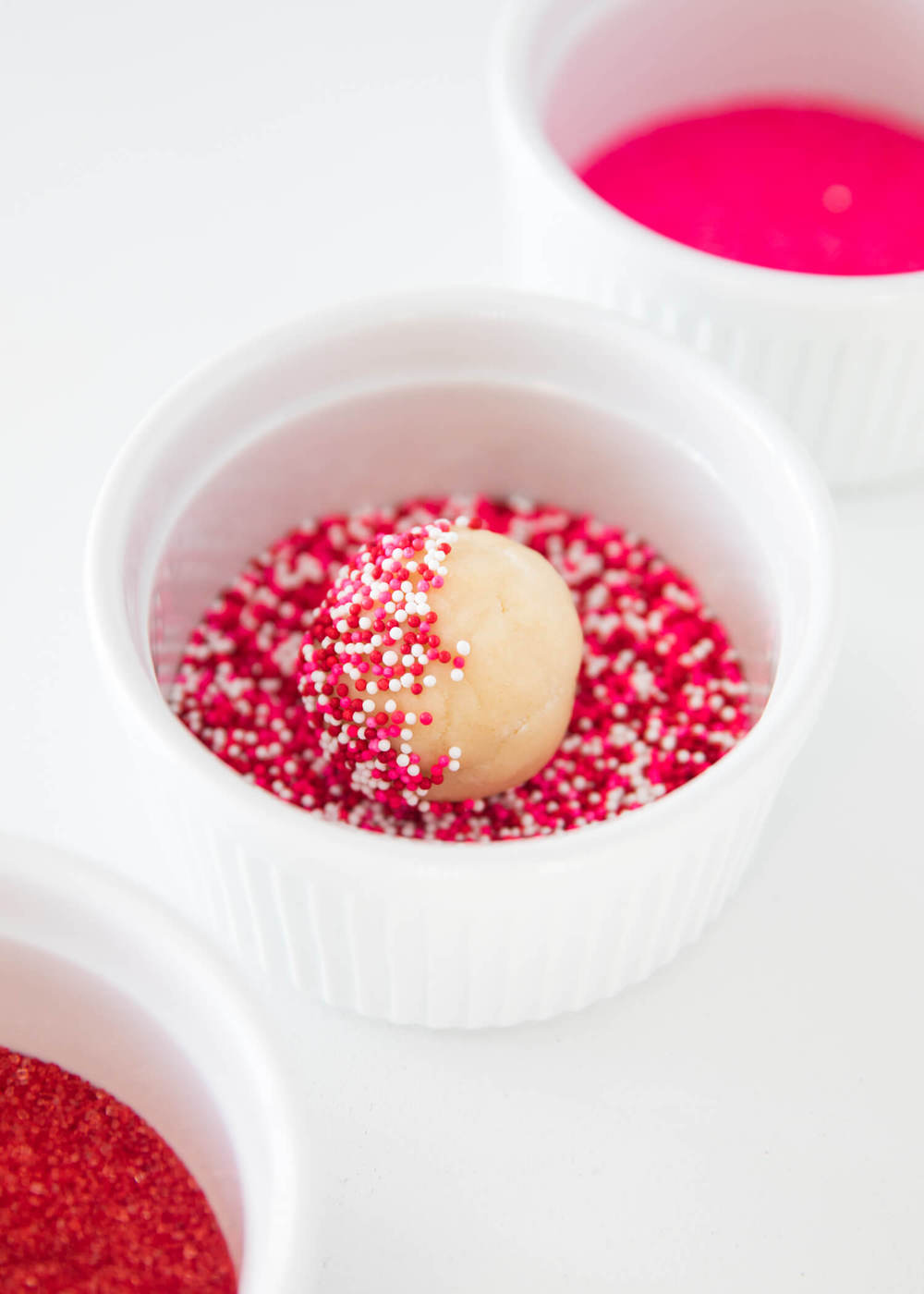 Rolling a sugar cookie dough ball into Valentines Day sprinkles.