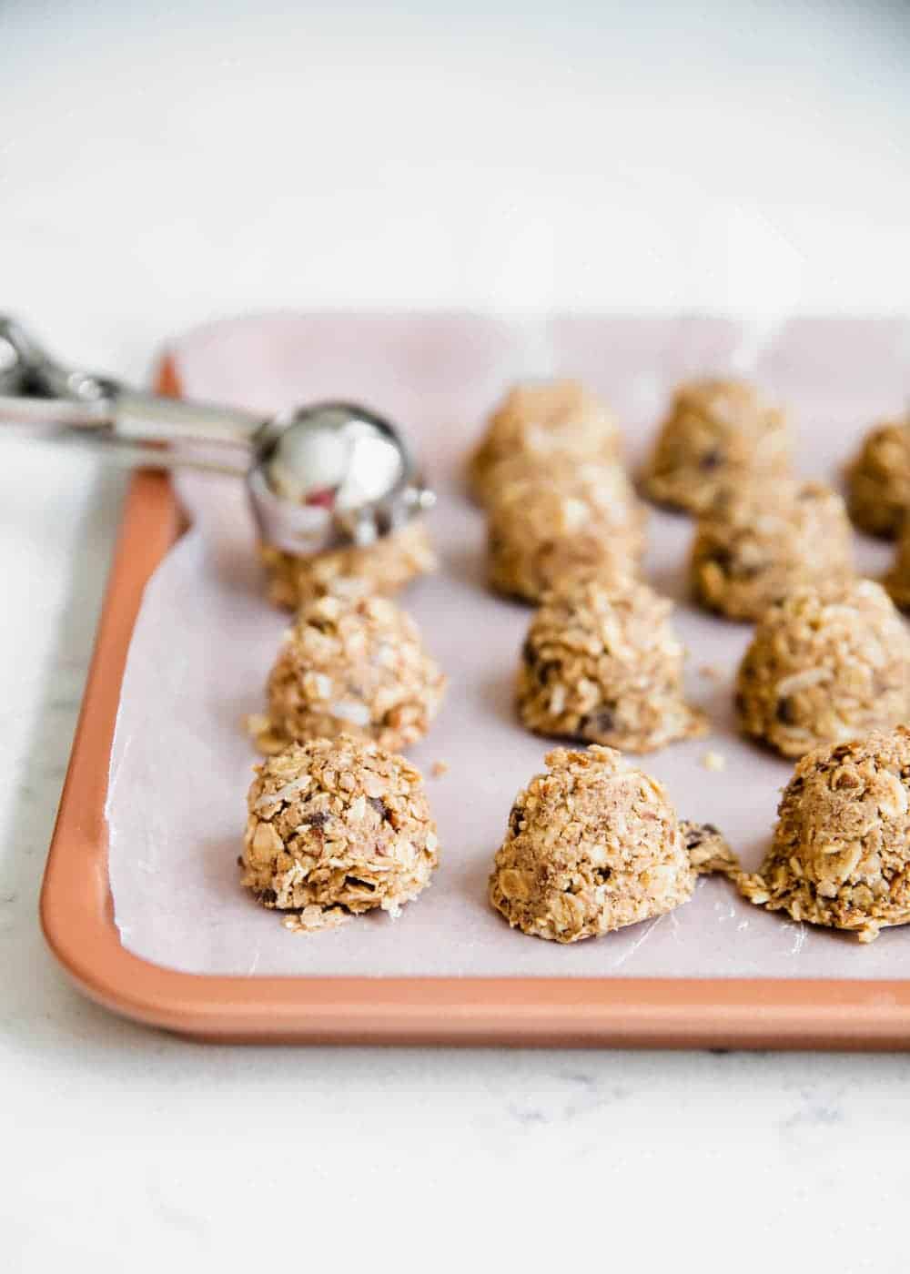 Scooping energy bites with a small cookie scoop onto a parchment lined baking sheet.