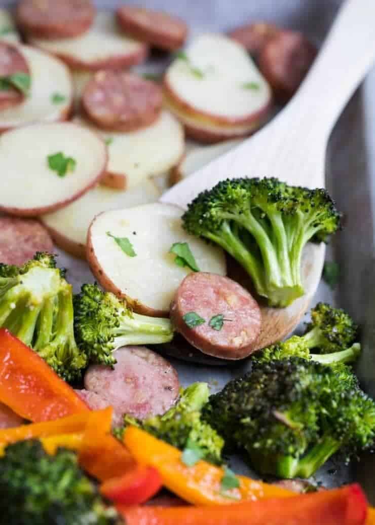 sausage and veggies on a baking sheet with a wooden spoon 