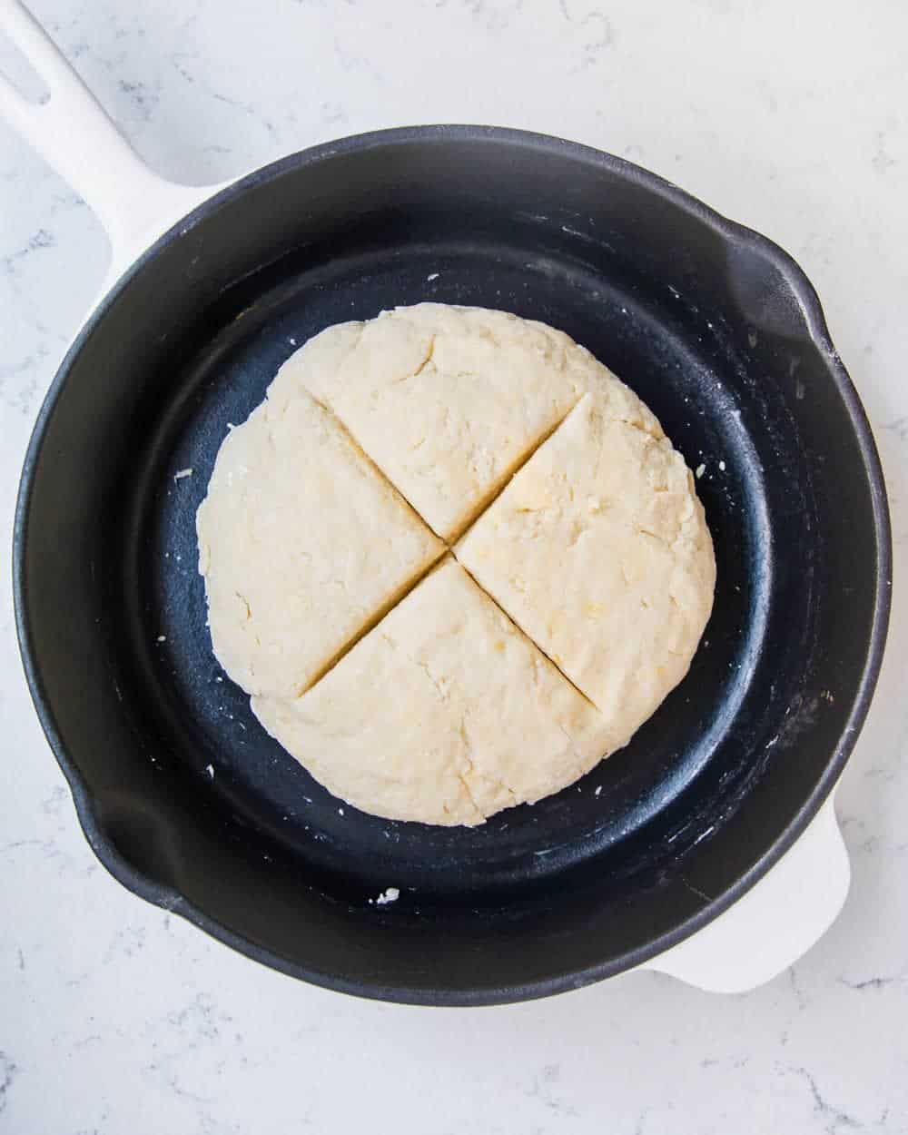Unbaked Irish soda bread scored with a cross in a cast iron baking dish.