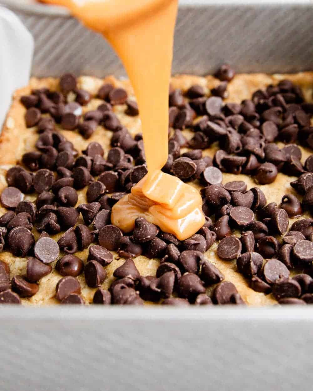 Pouring caramel on top of oatmeal bars with chocolate chips.