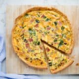 ham and cheese quiche on a cutting board with a slice cut out