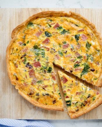 ham and cheese quiche on a cutting board with a slice cut out