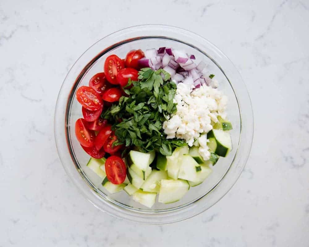 Ingredients for cucumber tomato salad in glass bowl.