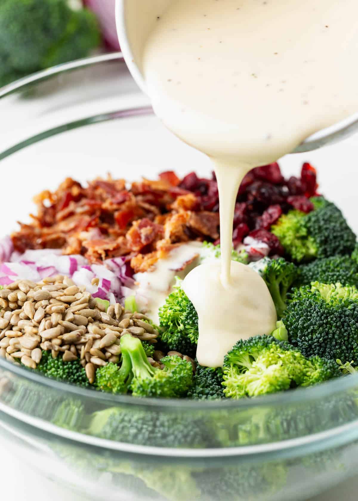 Dressing being poured over broccoli salad with bacon.