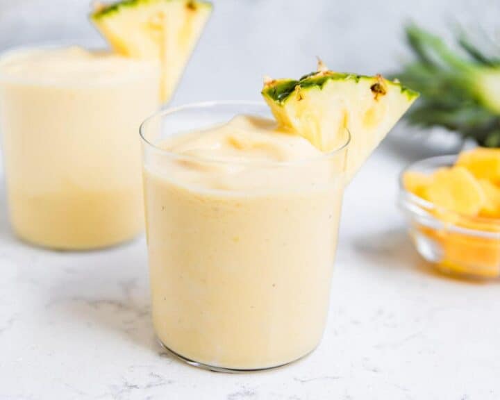 pineapple smoothie in a clear glass with a fresh pineapple slice