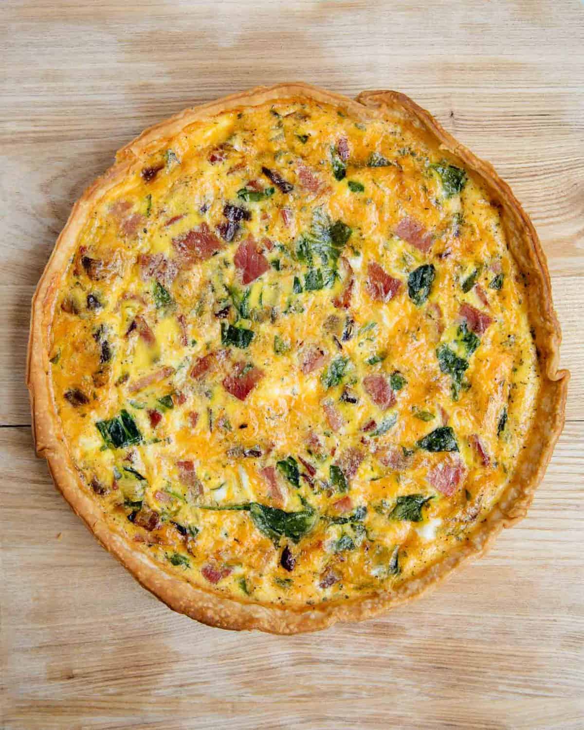 Baked ham and cheese quiche on a wood cutting board.