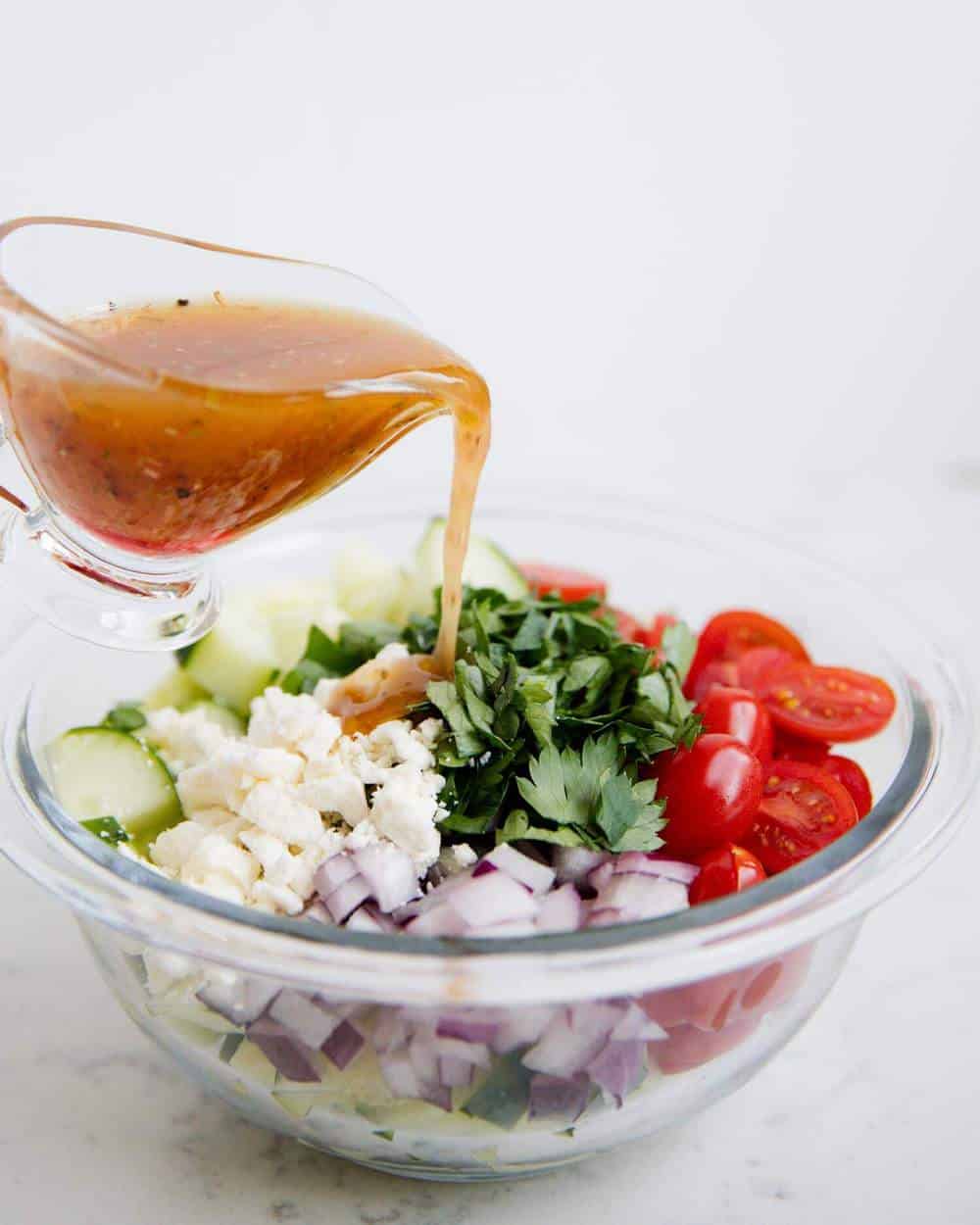 Pouring vinaigrette over cucumber tomato salad.