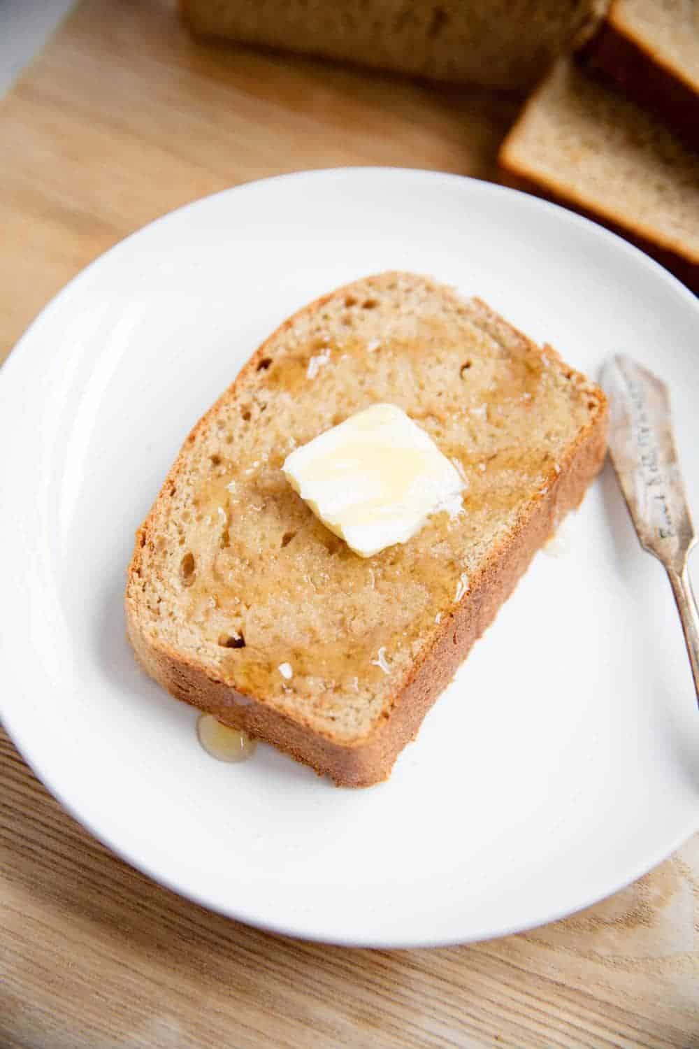 Slice of homemade wheat bread topped with butter and honey.