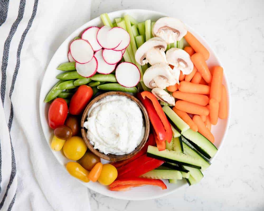 Dill dip and fresh vegetables on a white plate.