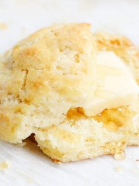 A sliced biscuit with butter and honey