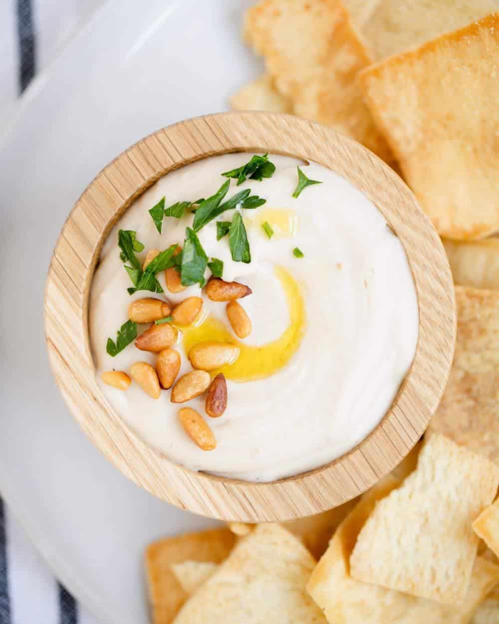 bowl of white bean hummus topped with toasted pine nuts and olive oil 