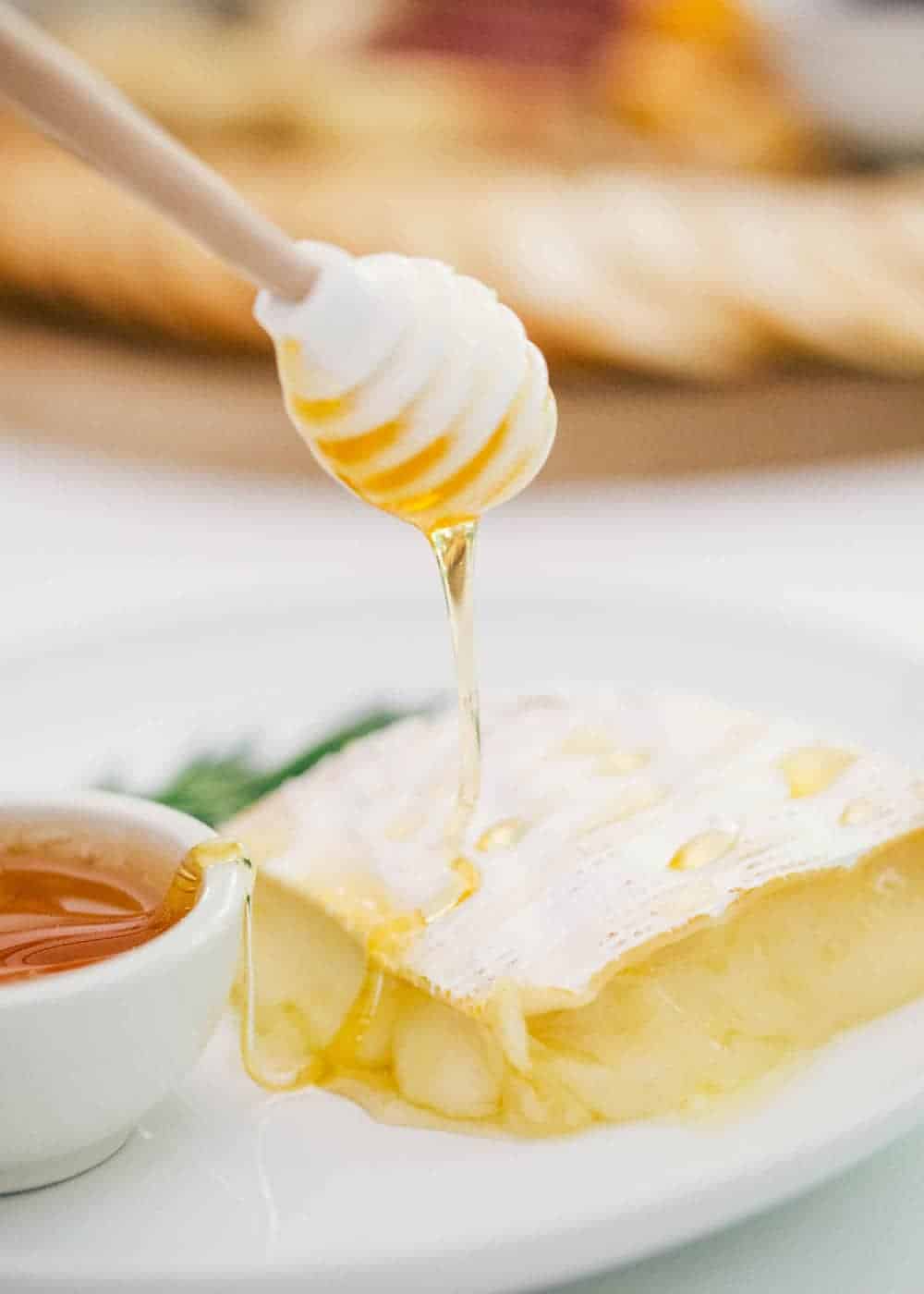 Using a honey dipper to drizzle honey onto baked brie.