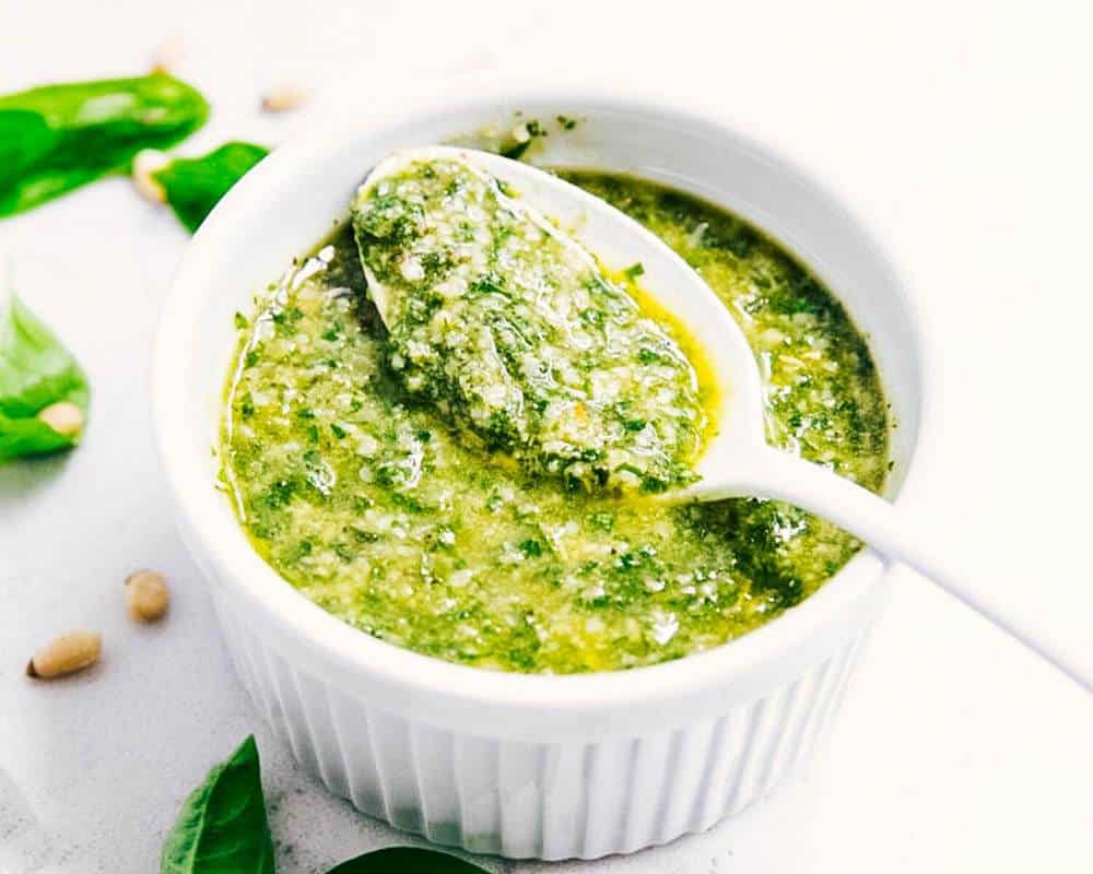 Basil pesto in a white bowl with a spoon.
