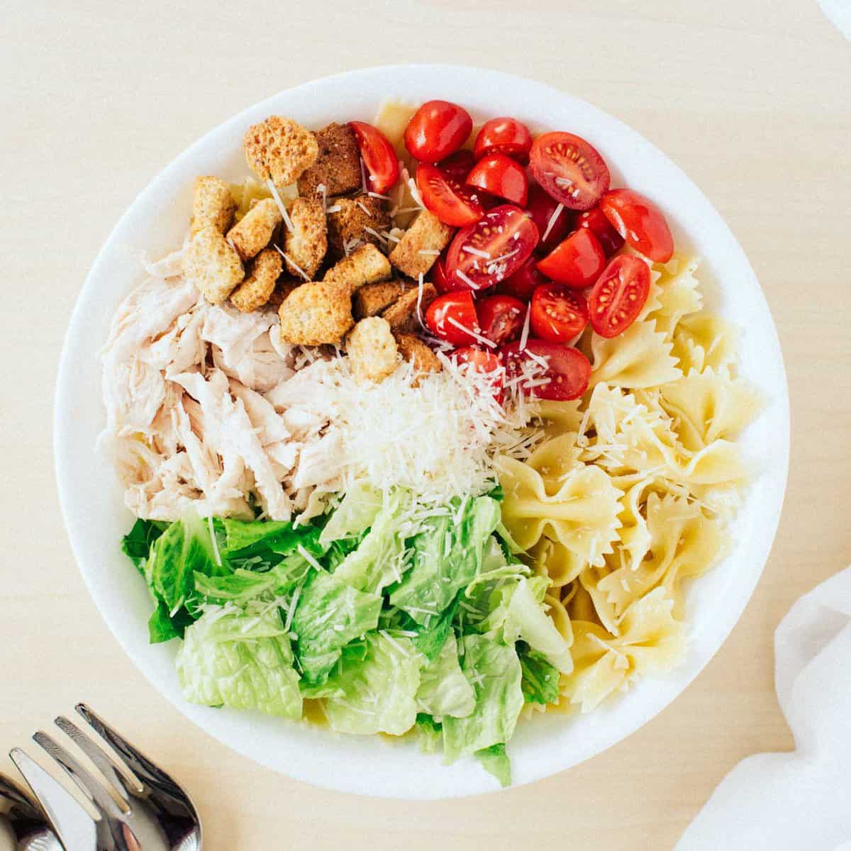 Ingredients for caesar pasta salad in large white bowl.