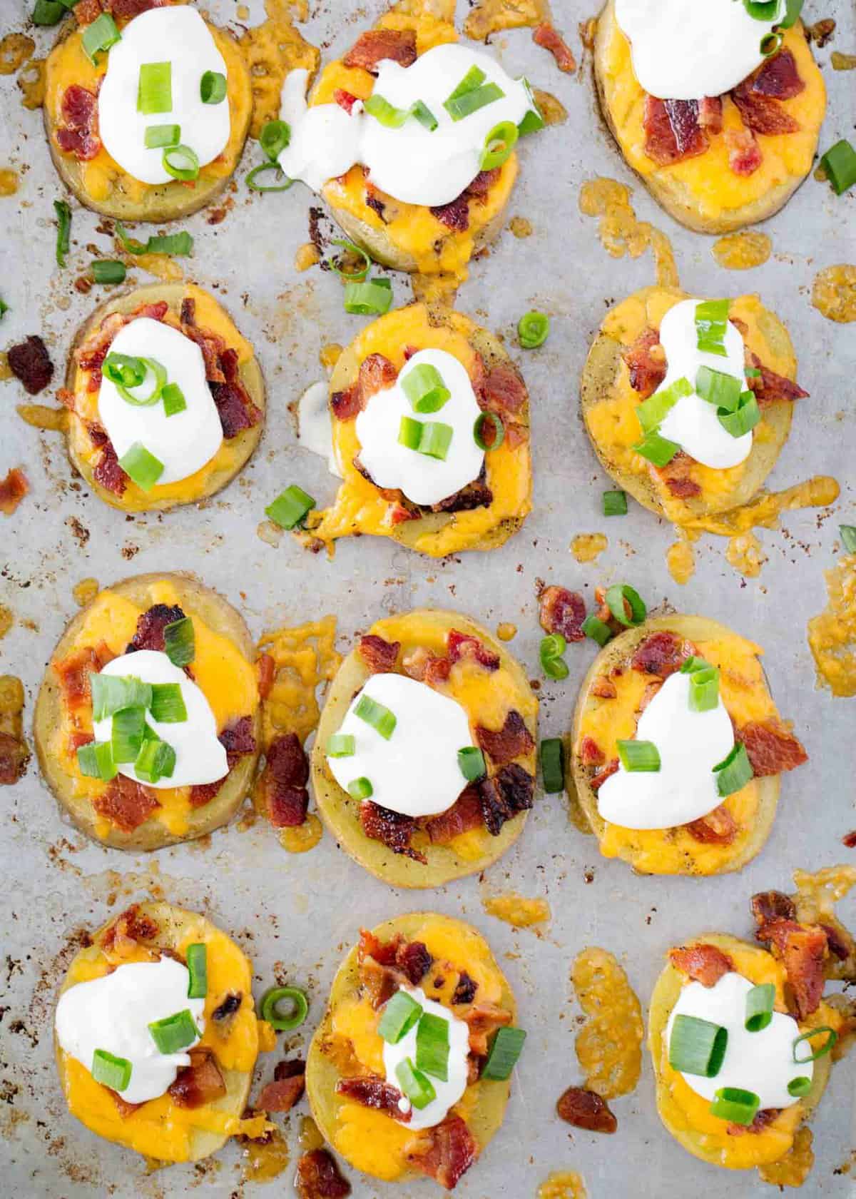 Potato skins on a baking sheet topped with sour cream and green onions.