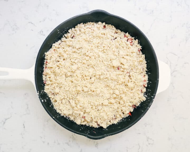 crumble topping on top of fresh strawberries and rhubarb in skillet 