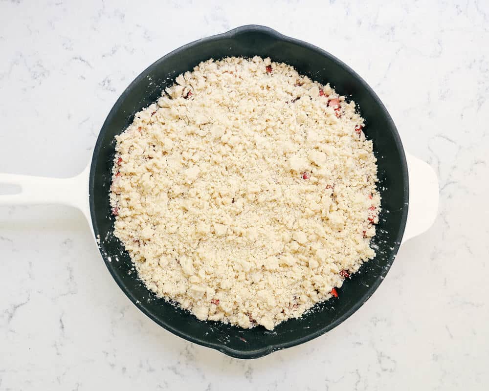 Crumble topping on top of fresh strawberries and rhubarb in skillet.