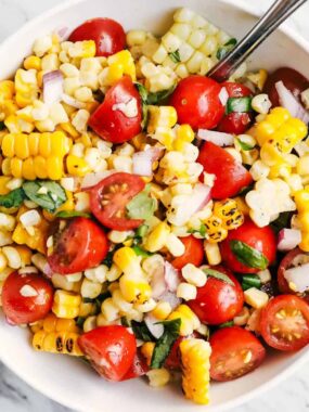 Top down photo of fresh corn and tomato salad in a white serving bowl with basil.