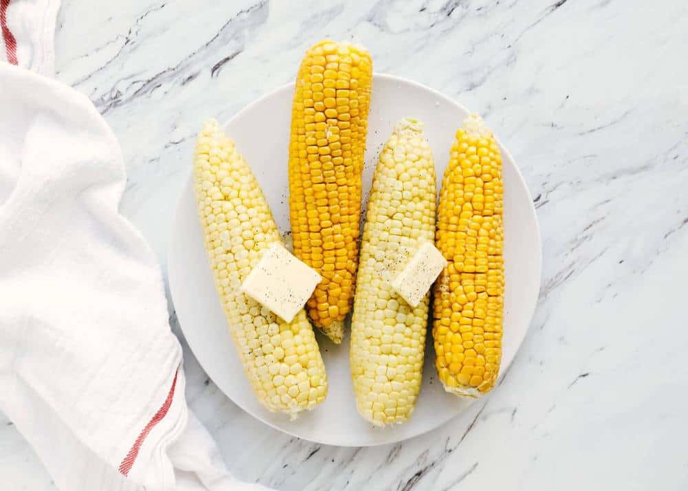 Corn on the cob on a white plate with butter on top.
