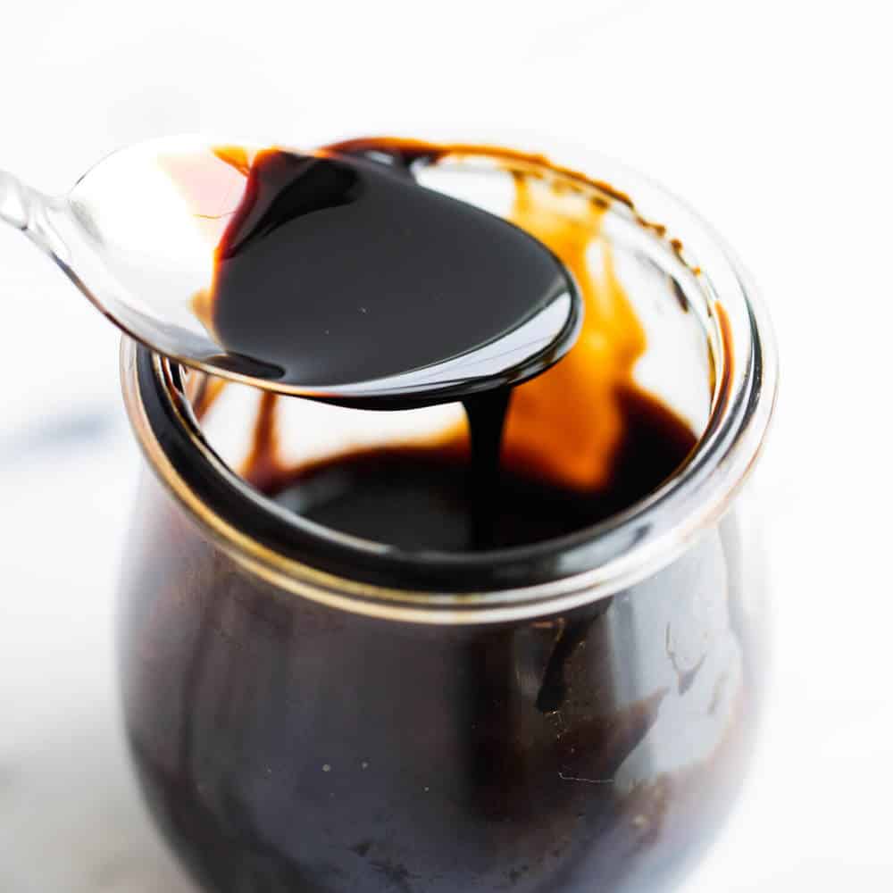 Spoonful of balsamic glaze dripping into a glass jar.