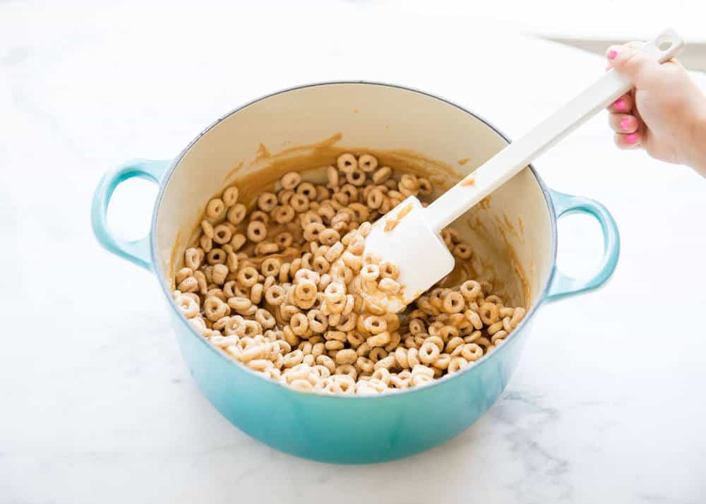 Stirring together peanut butter mixture and cheerios in a large pot.