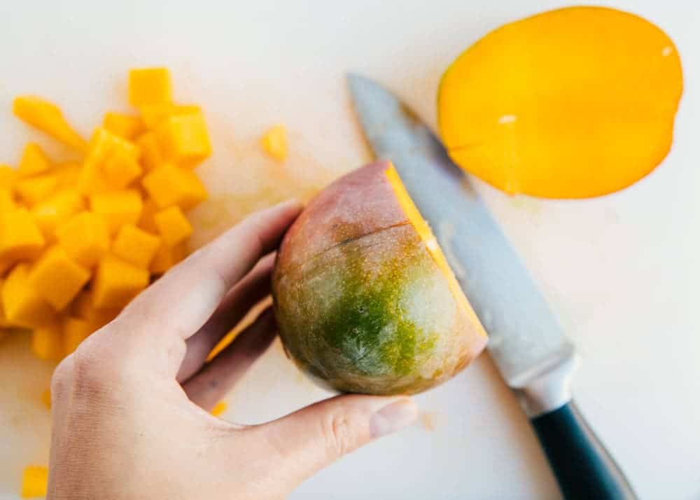 Slicing sides off of a mango on a cutting board.