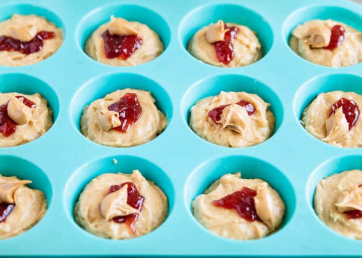 muffin batter in pan with strawberry jam and peanut butter on top 