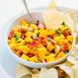 dipping a chip into a bowl of mango salsa