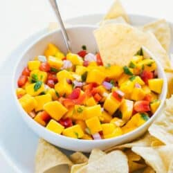 dipping a chip into a bowl of mango salsa