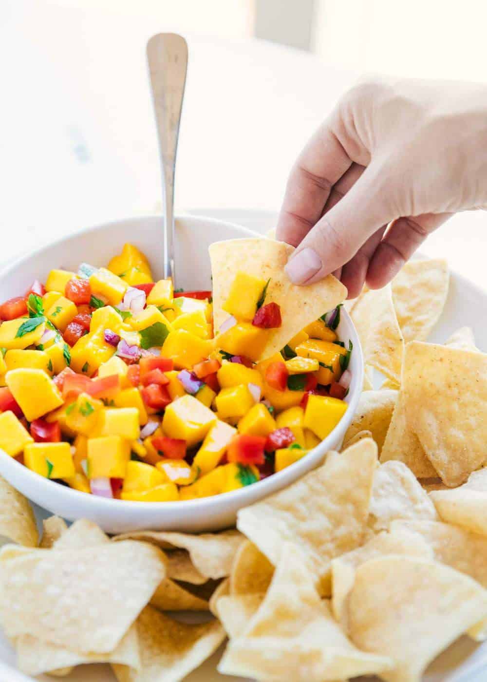 Dipping a tortilla chip in a bowl of mango salsa.