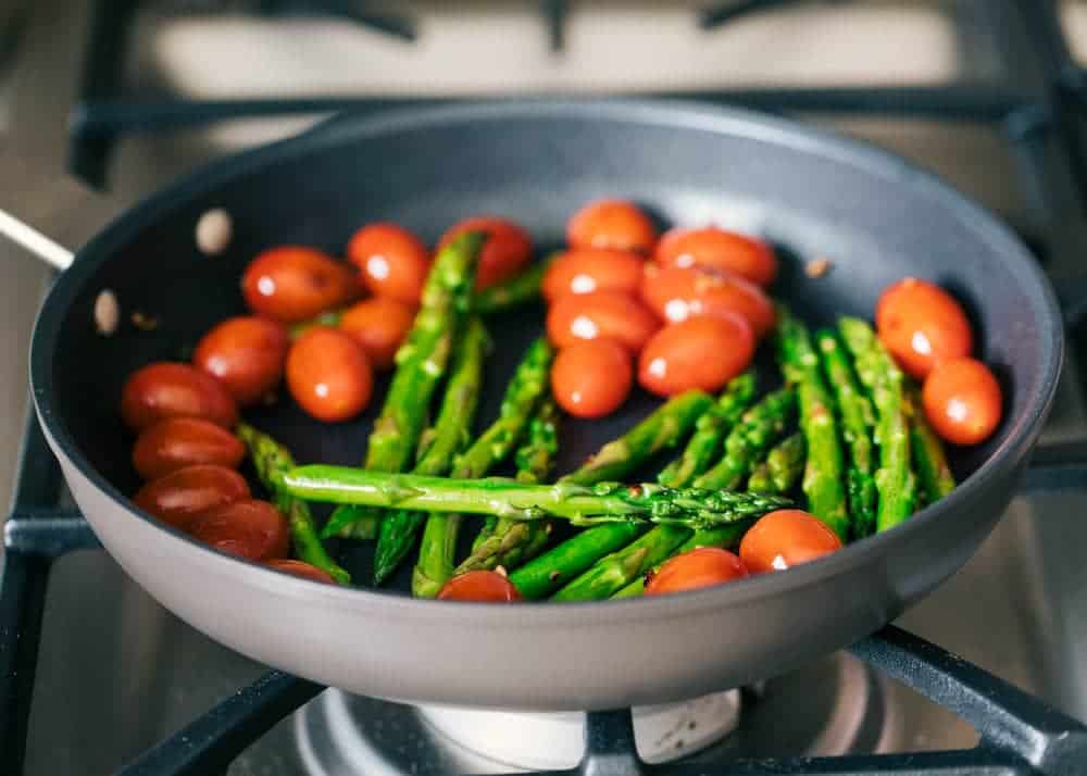 Sautéing tomatoes and asparagus on skillet.