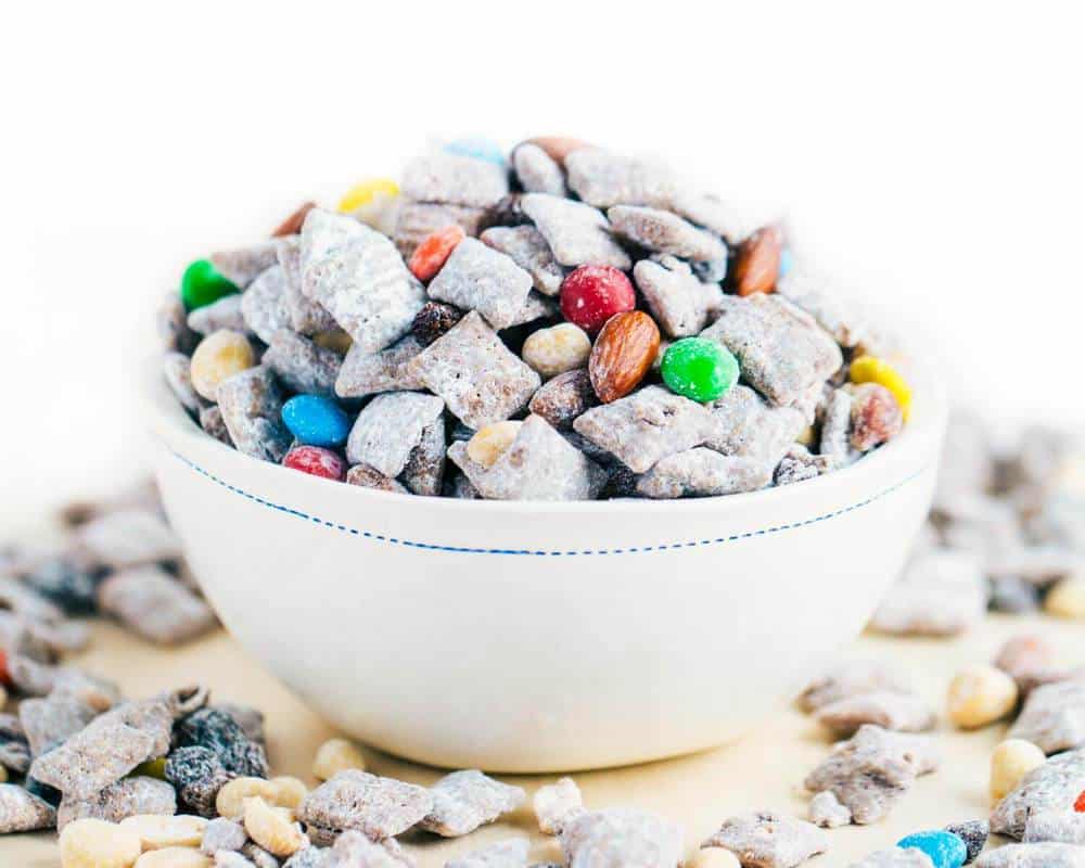 Trail mix muddy buddies in a white bowl.