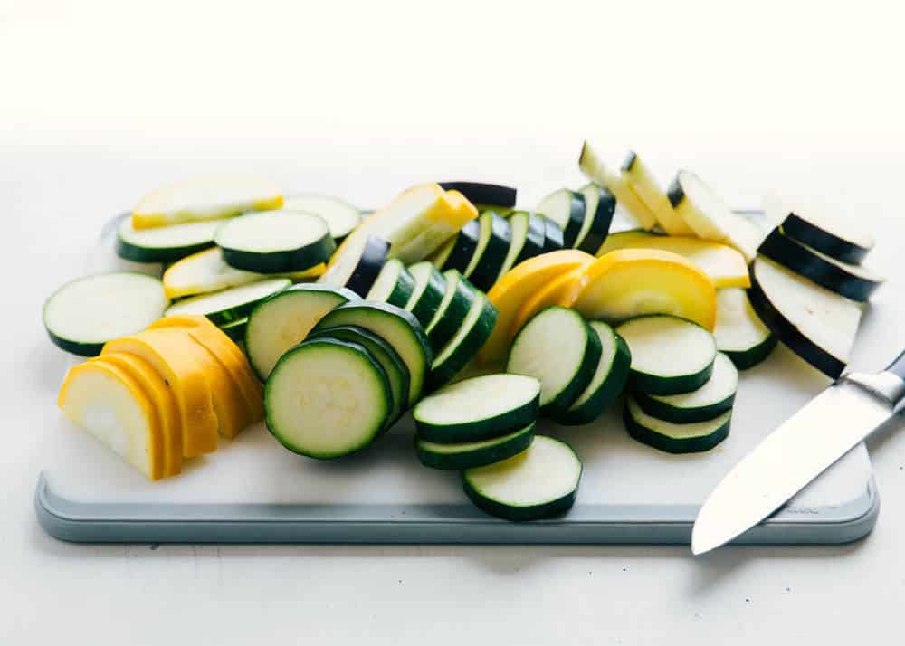 Sliced zucchini squash on a white cutting board.