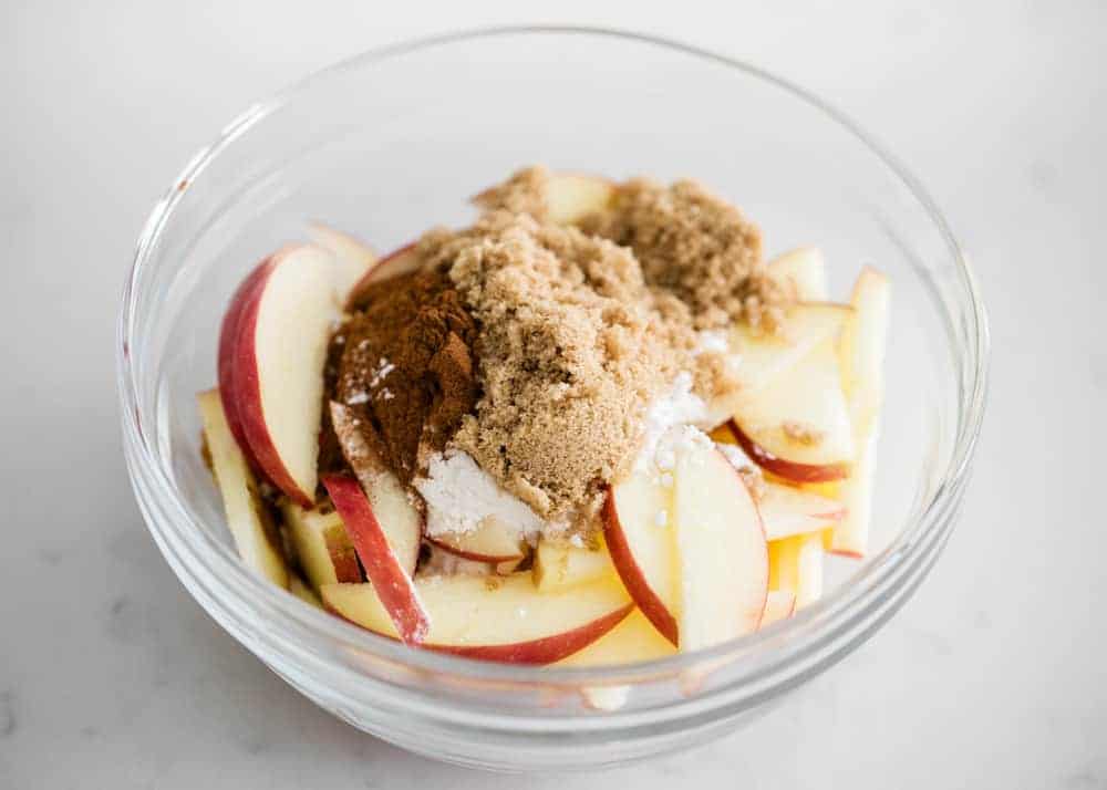 Apples and brown sugar in a glass bowl.