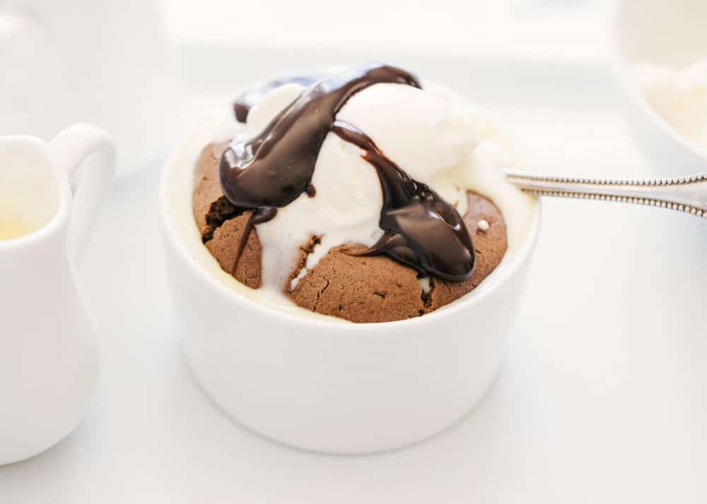 Chocolate souffle in ramekin with ice cream and chocolate sauce.