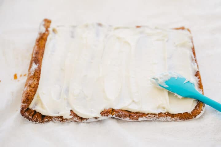 Delicious layers of fluffy pumpkin cake and sweet cream cheese filling swirled together to make the ultimate treat! This easy pumpkin roll is perfect to serve during the fall season. spreading cream cheese filling on pumpkin cake