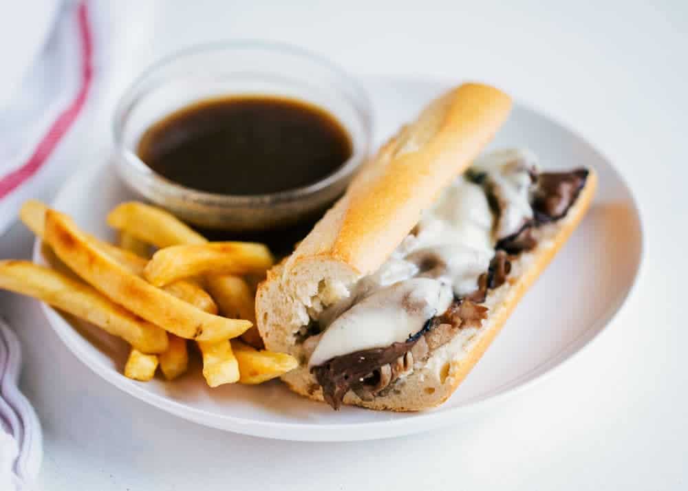 French dip sandwich on a plate with au jus and fries.