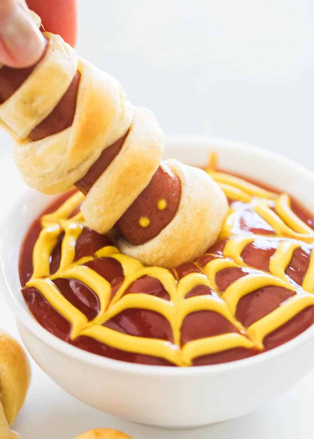 These mummy hot dogs are the easiest Halloween appetizer that takes only 2 ingredients to make! So fun, festive and delicious. Serve with spooky spider web sauce for the ultimate Halloween experience! Dipping hot dog mummy into spider sauce.