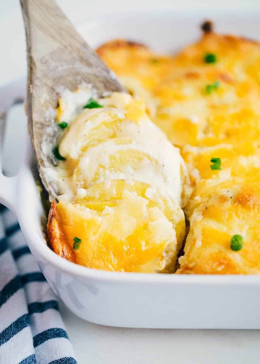 cheesy scalloped potatoes in a baking dish with a wooden spoon 