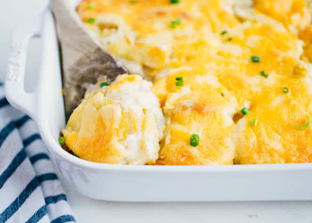 scalloped potatoes in a baking dish with a wooden spoon 