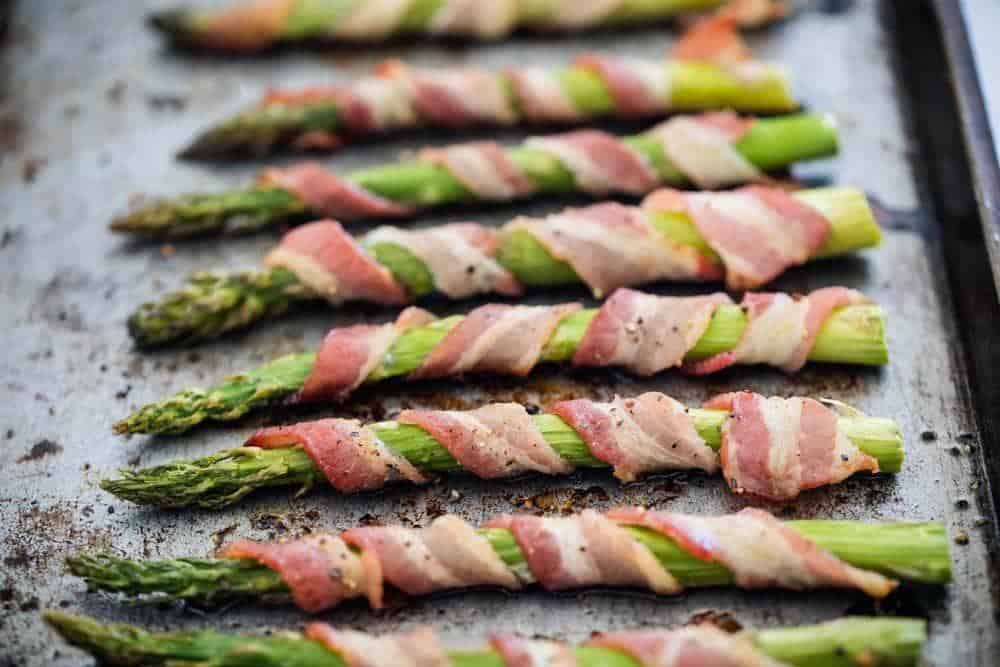 Asparagus wrapped in bacon on baking sheet.