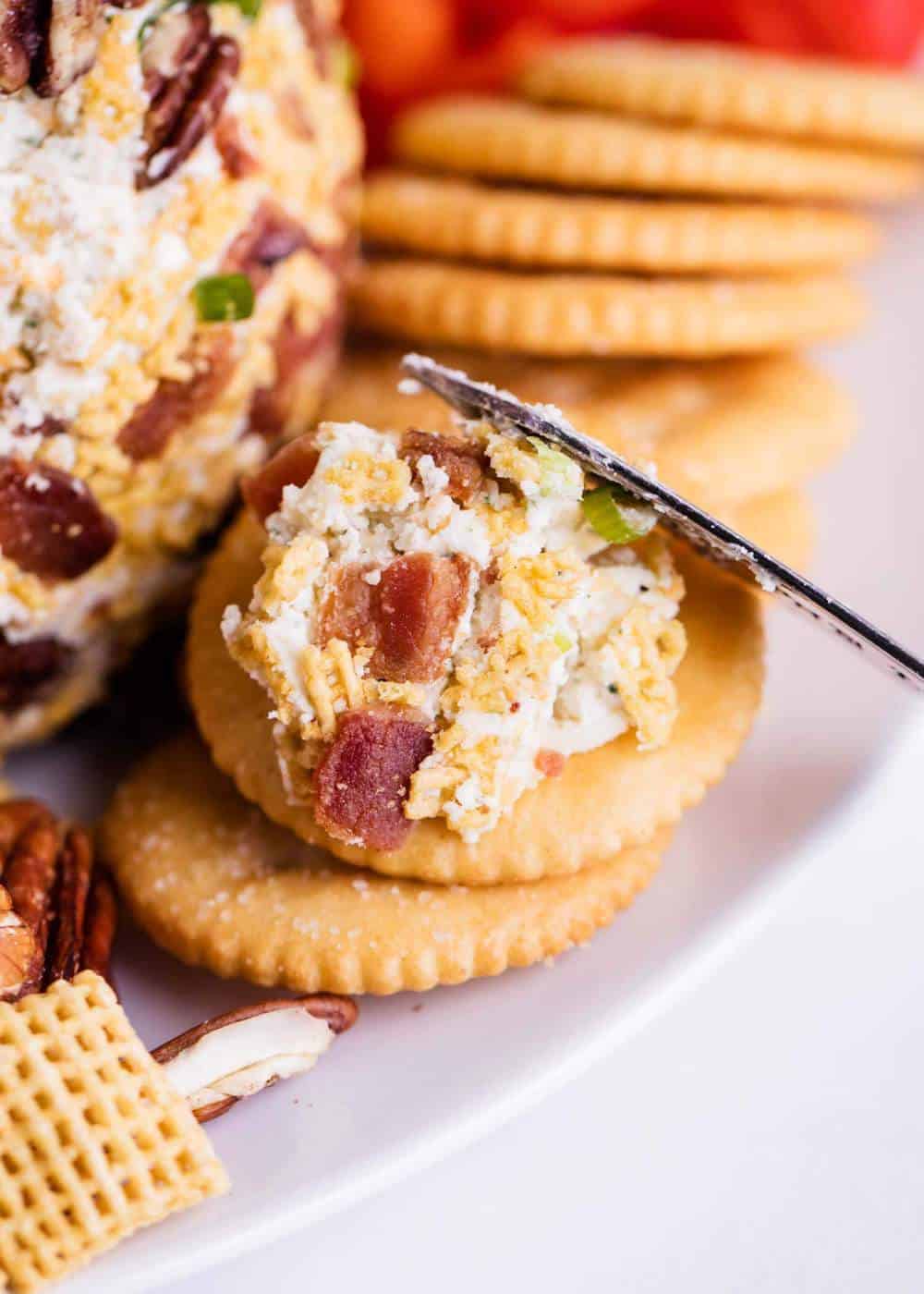 Spreading bacon cheese ball on top of a cracker with a knife.