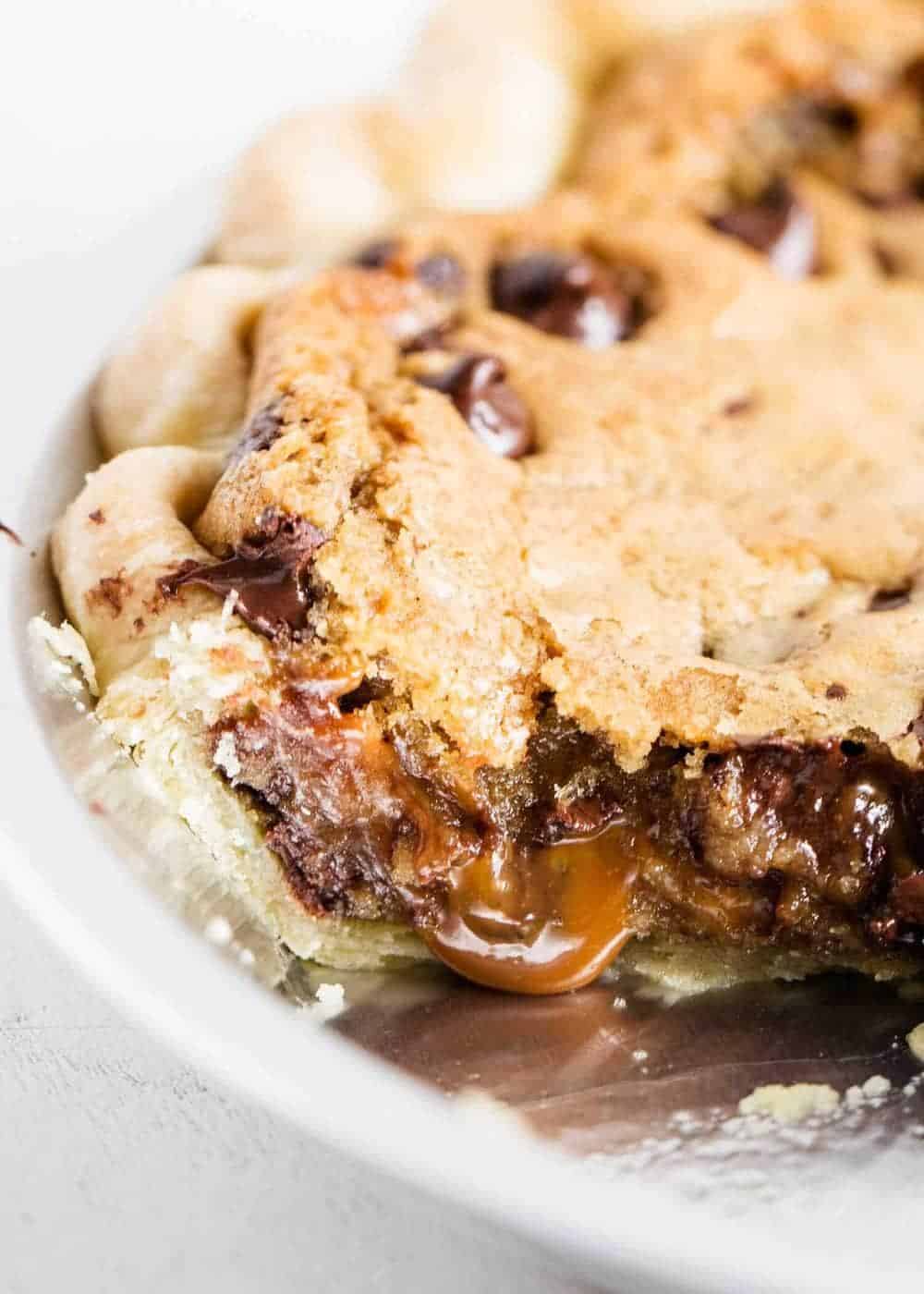 A close up of chocolate chip cookie pie with caramel oozing out.