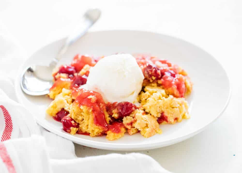 Cherry dump cake on a plate with a scoop of vanilla ice cream.